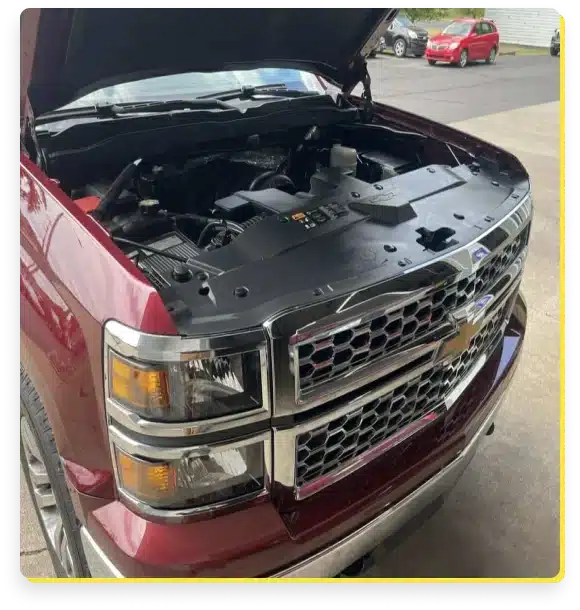 At Jerry's Automotive. A red Chevrolet truck, its hood open for some GM car care, reveals the engine. The truck is parked on a driveway with other vehicles visible in the background.