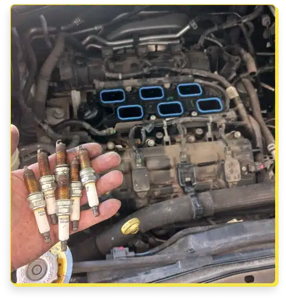 At Jerry's Automotive. A person holds five used spark plugs in their hand above an open car engine. The engine is partially disassembled, exposing the intake manifold. Nearby, tools and various components suggest ongoing engine repair services aimed at restoring peak performance.