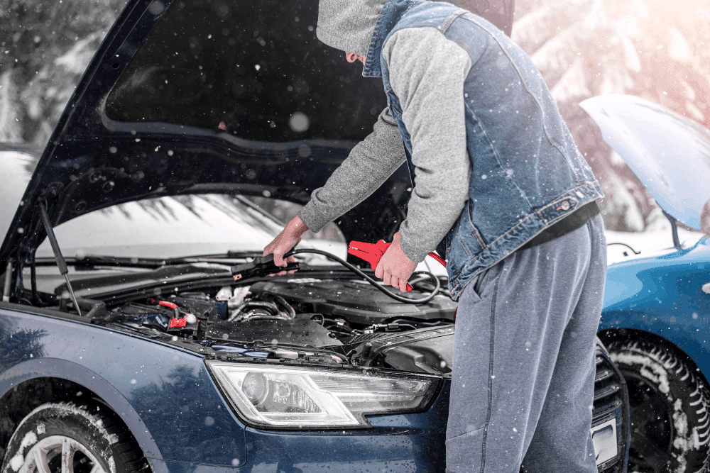 Winter car care, auto repair in Lansing, MI by Jerry’s Automotive. Image of a driver jump-starting a vehicle in snowy conditions, highlighting cold-weather battery service and electrical system reliability.