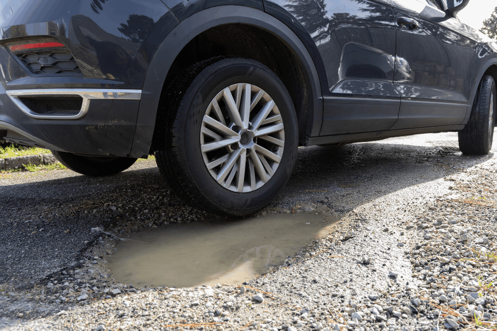 Steering and suspension check, auto repair in Lansing, MI by Jerry’s Automotive. Image of a vehicle tire hitting a pothole, highlighting risks to suspension, alignment, and overall driving safety.