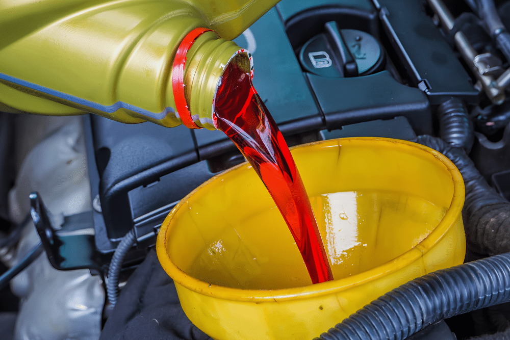 Oil Change in Lansing, MI at Jerry's Automotive. Close up view of oil being poured from a gold bottle through a yellow funnel into a car engine during a oil change service.