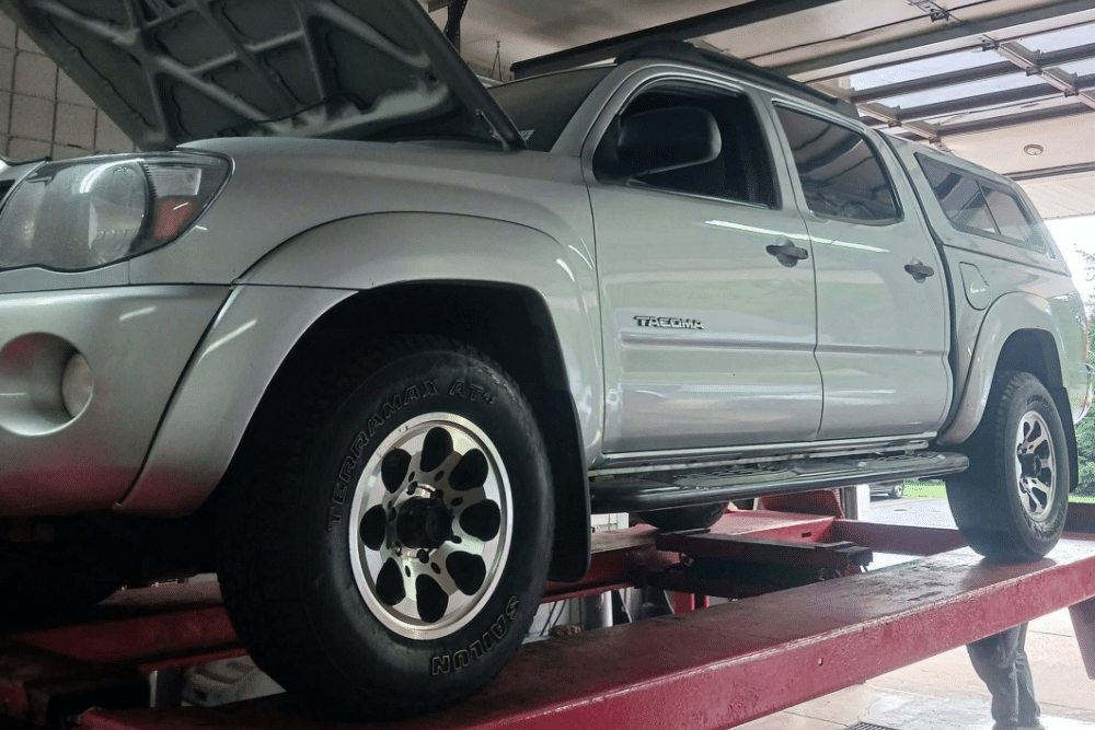 Pre-Road Trip Car Maintenance in Lansing MI at Jerry's Automotive. Close up view of pickup truck with its hood open sits on a red alignment lift inside a garage during a pre-road trip maintenance check.
