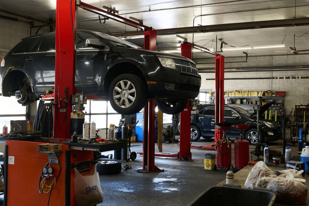 Auto Repair Near MSU in Lansing with Jerry's Automotive. Lincoln MKX raised on a red hydraulic lift inside a busy auto repair shop bay