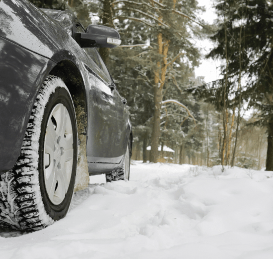 winter car care, auto repair in Lansing, MI at Jerry's Automotive. Close-up of a car equipped with winter tires driving through snow.